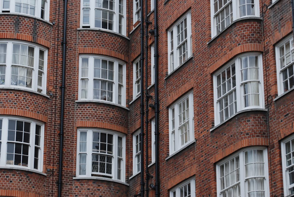 Photograph of a historic red brick residential building with multiple floors, large sash windows, and ornate white decorative elements along the upper windows and roofline, located on a quiet street u
